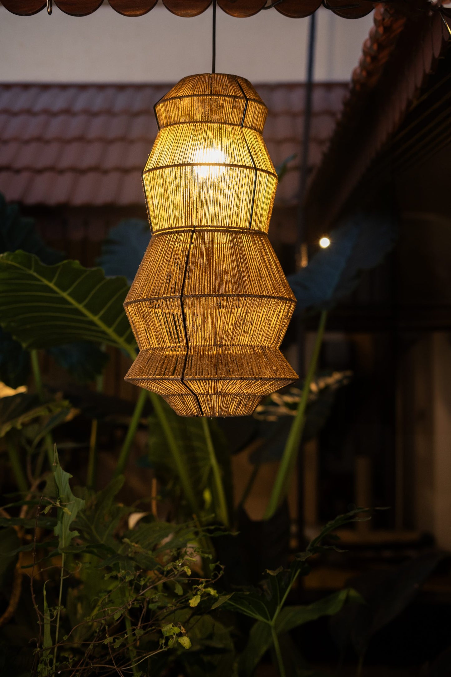 A Japanese inspired 3-tier chandelier made of wicker with a warm light hanging outdoors.