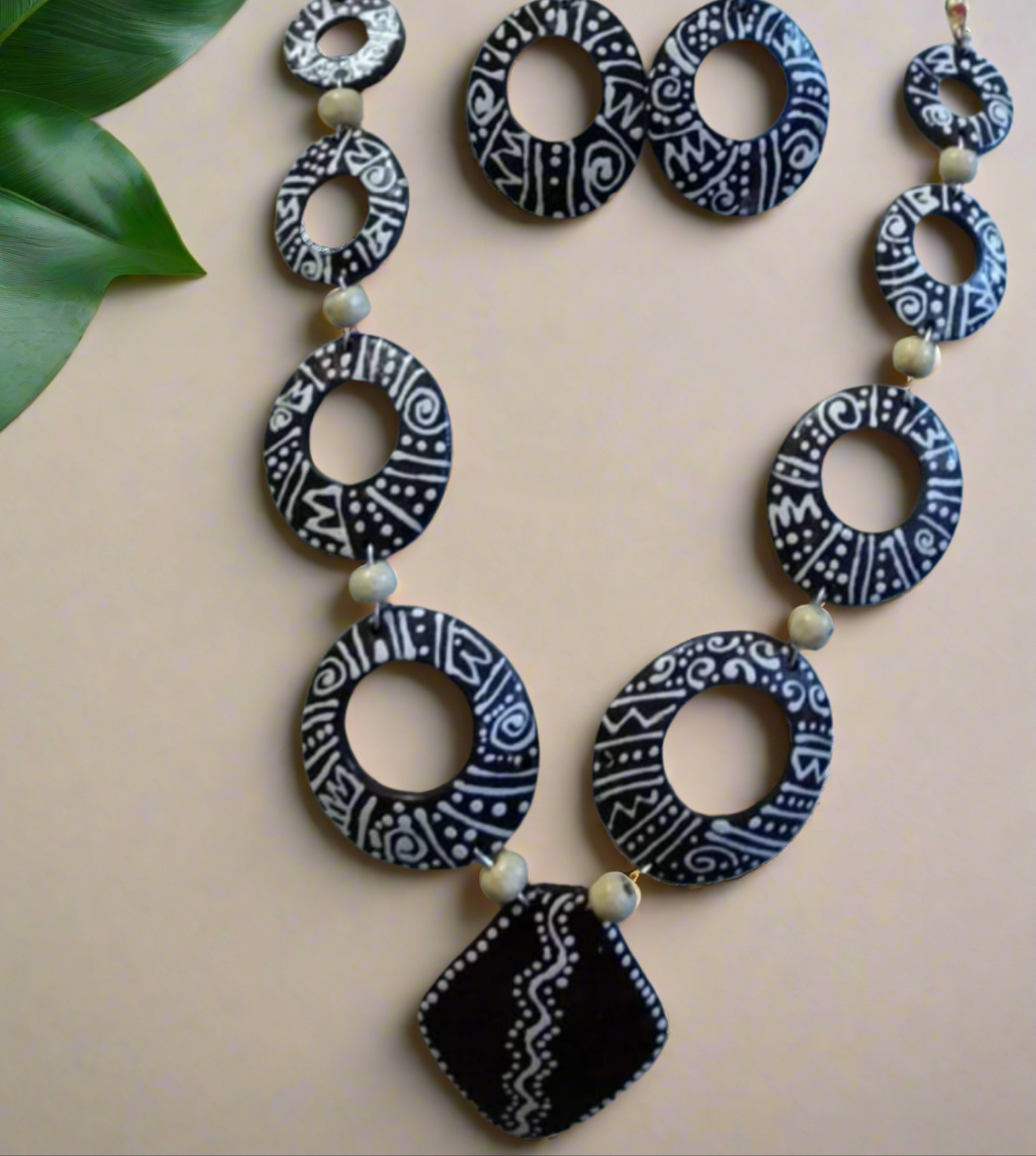 A necklace set with oval handcarved and chained pieces in black, white, and beige colors, displayed on a mannequin bust, with coconut shell earrings included.