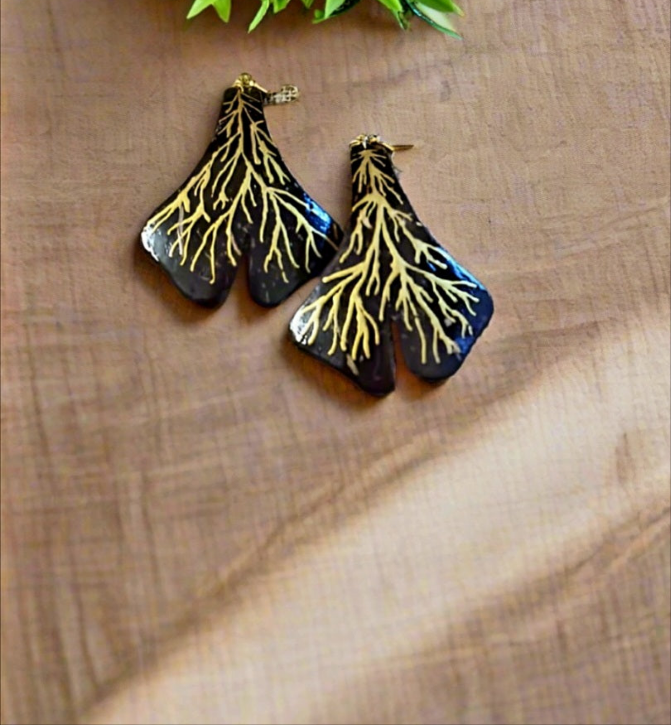 A pair of earrings designed to resemble tree roots, placed on a beige fabric surface.