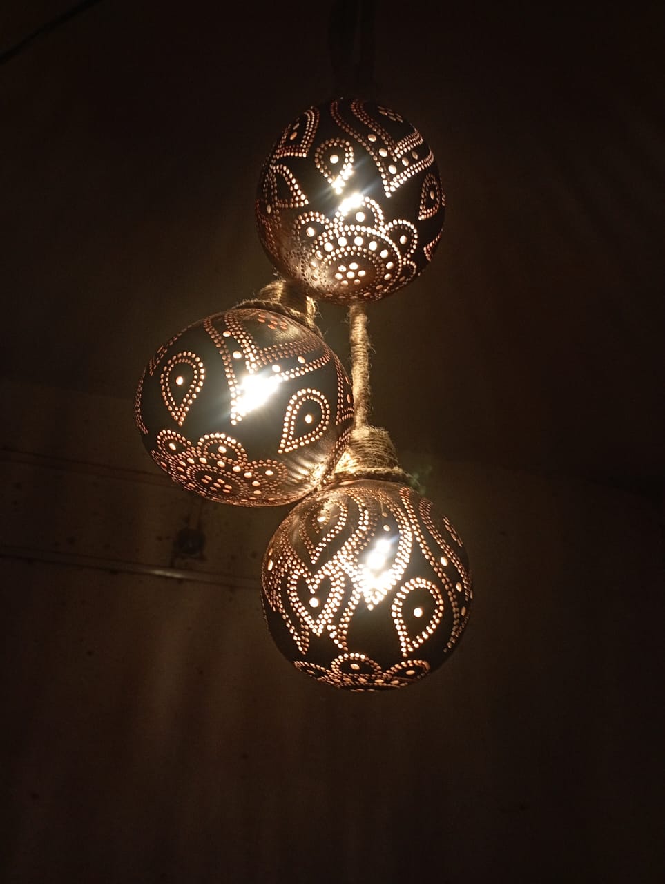 Three hanging lamps made of coconut shell with floral patterns, illuminated, set against a natural background.