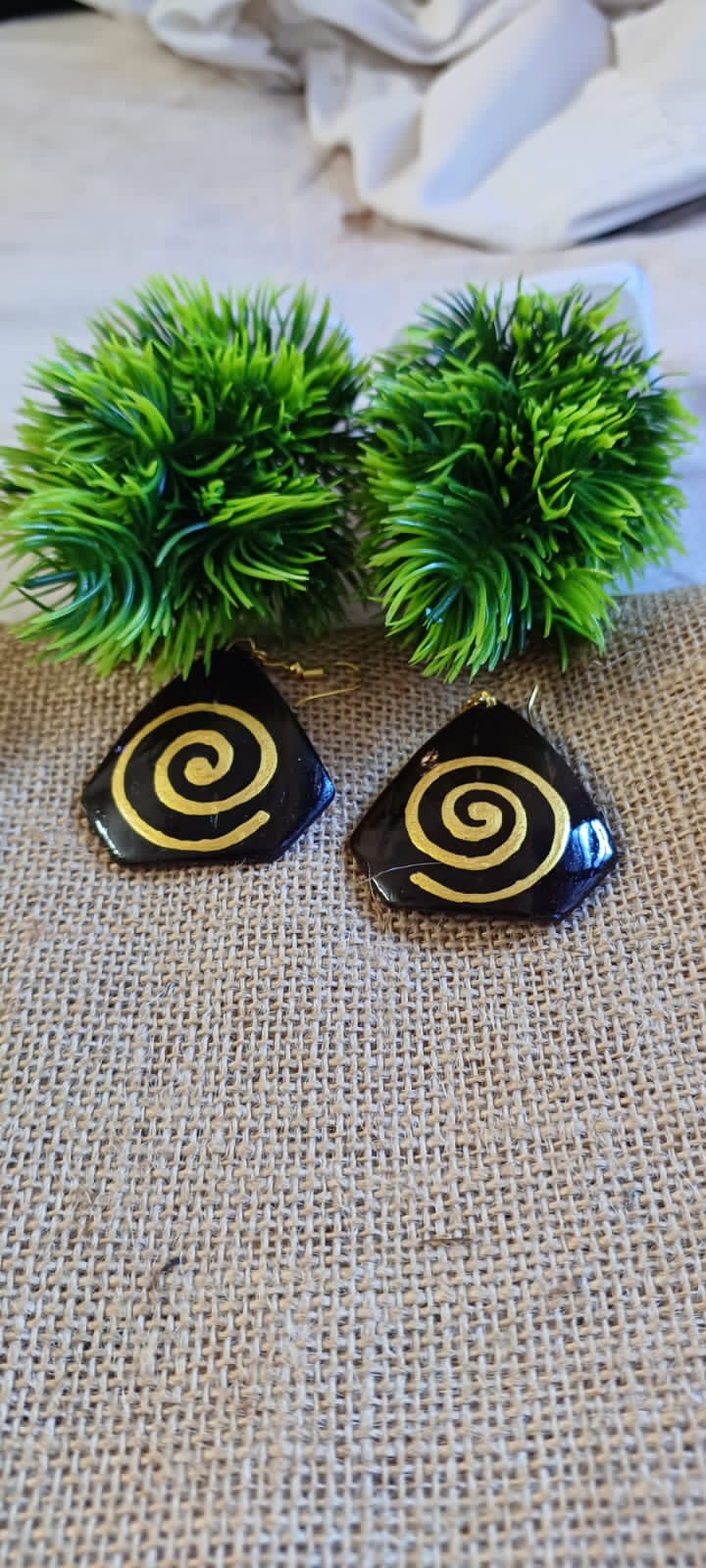 A pair of spiral patterned earrings on a burnt orange textured background, with green plant-like embellishments.