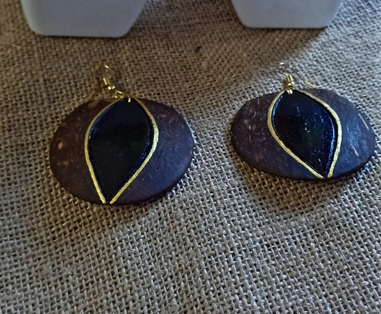 A pair of round coconut shell earrings, dark brown in color with a gold accent on the edge.