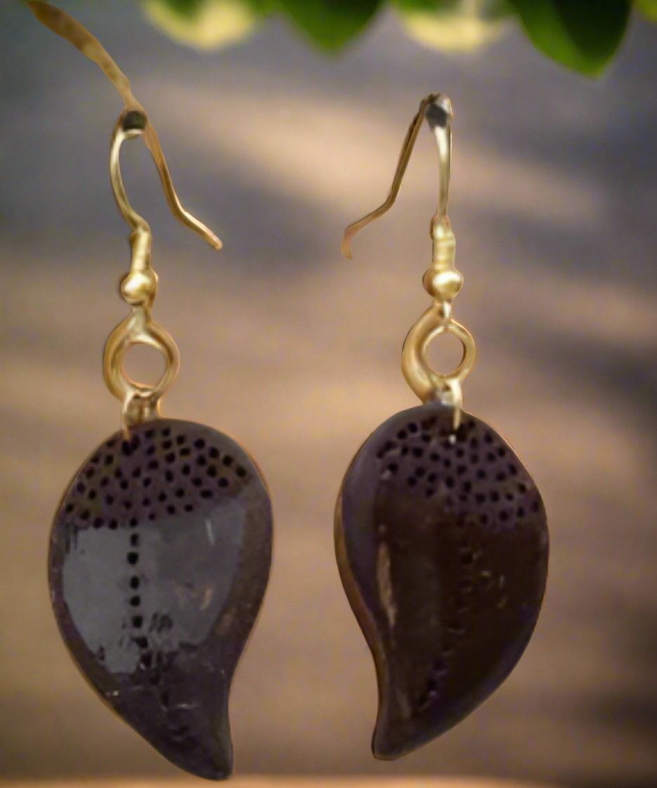 A set of handcrafted jewelry featuring leaf-shaped charms and coconut shell earrings, displayed on a wooden surface with a plant background.