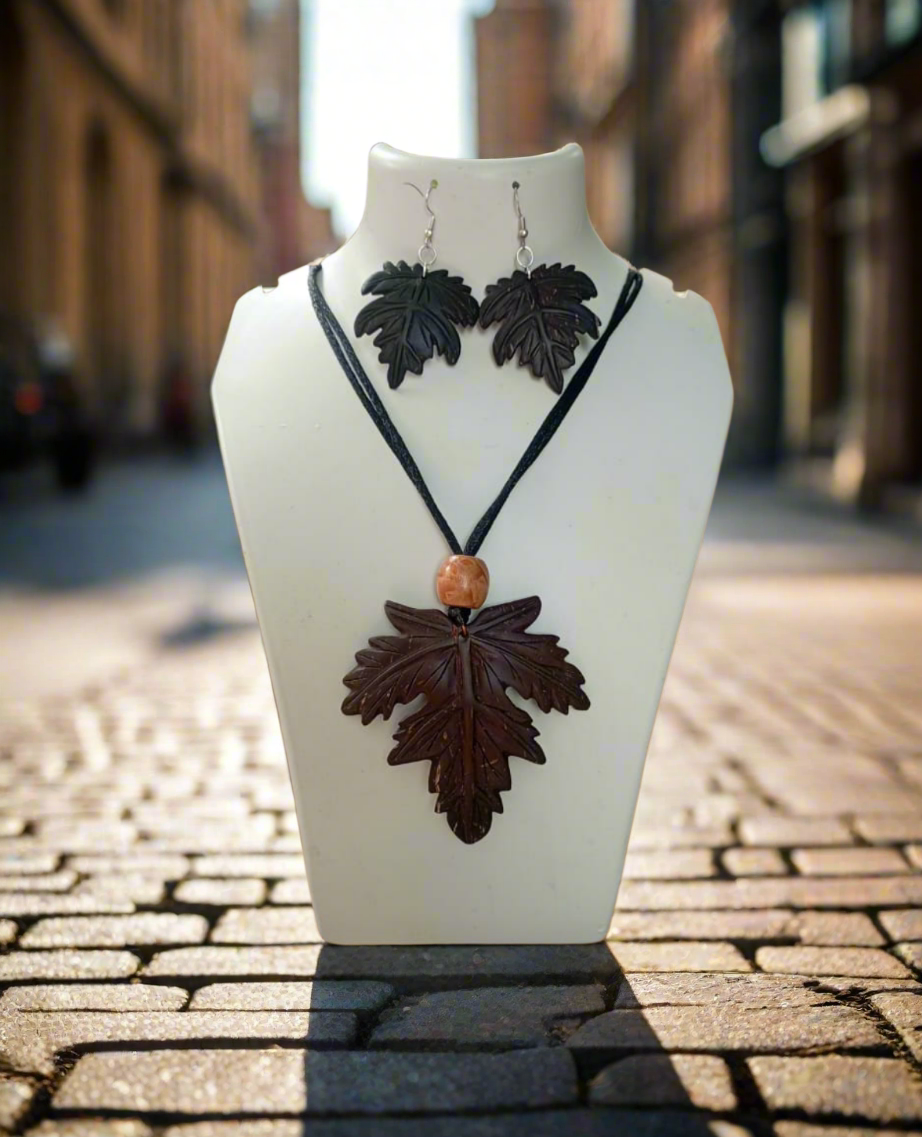 A pendant set featuring a maple leaf design, displayed on a mannequin bust with coconut shell earrings and a necklace.