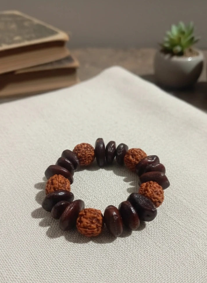 Bracelet made of brown and orange beads on a textured surface with books and a plant in the background.