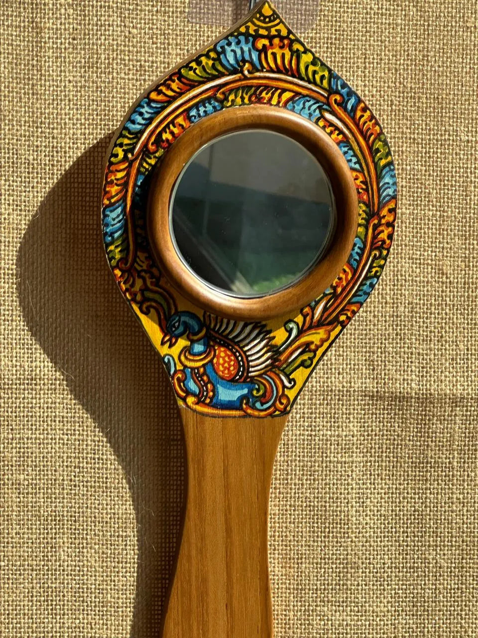 Decorative hand mirror with wooden handle and colorful floral design on a textured beige background
