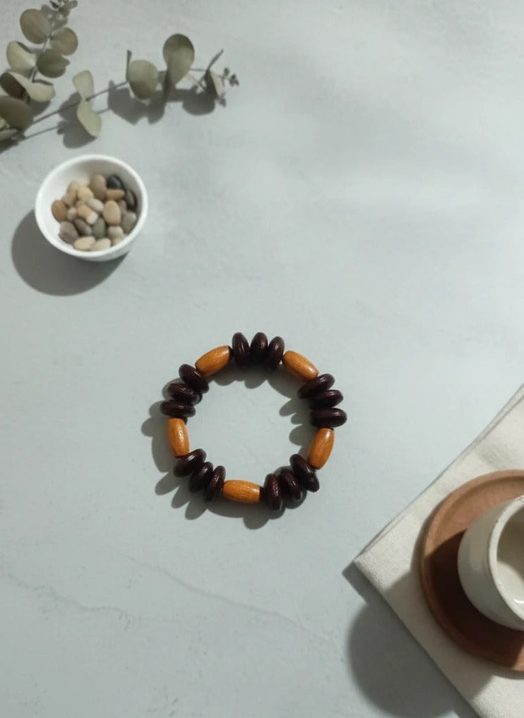 Wooden bracelet on a light gray surface with a small bowl of stones and a plant in the background.