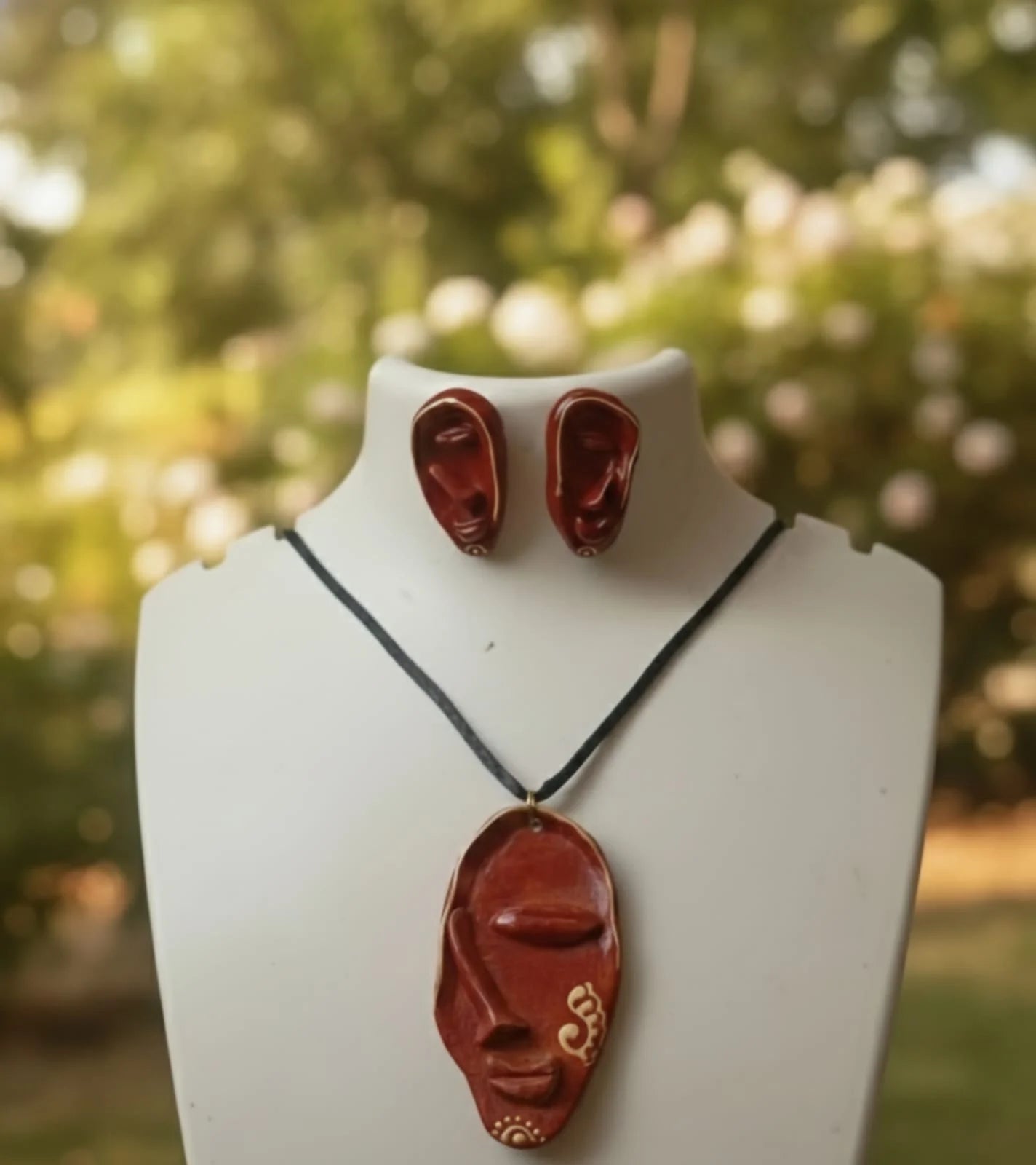 Red necklace and earrings on a mannequin bust with a blurred green background