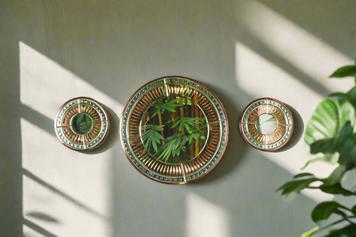 A set of three rose gold Venetian inspired 2D mirrors arranged on a wall, with one mirror reflecting a part of the wall and another reflecting a potted plant.