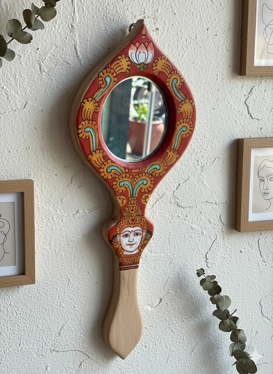 Decorative hand mirror with intricate designs on a textured wall.