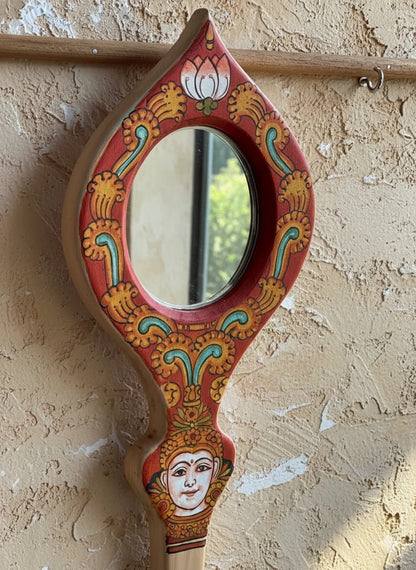 Decorative hand mirror with intricate designs on a textured wall