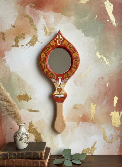 Decorative hand mirror with artistic handle on a shelf against a textured wall.