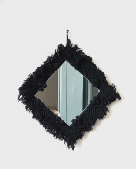 Black macramé-framed mirror on a white background