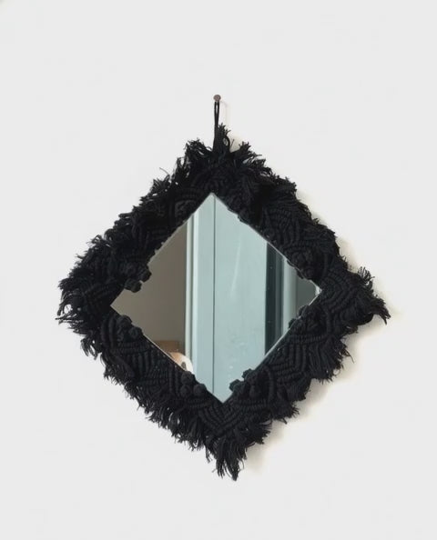 Black macramé-framed mirror on a white background