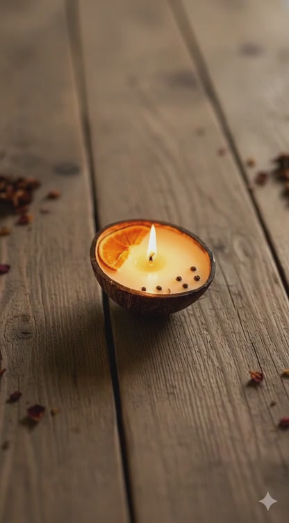Small candle in a coconut shell on a wooden surface with dried leaves.