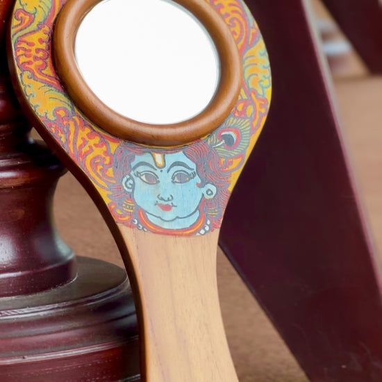 Decorative krishna hand mirror with colorful design on a dark surface