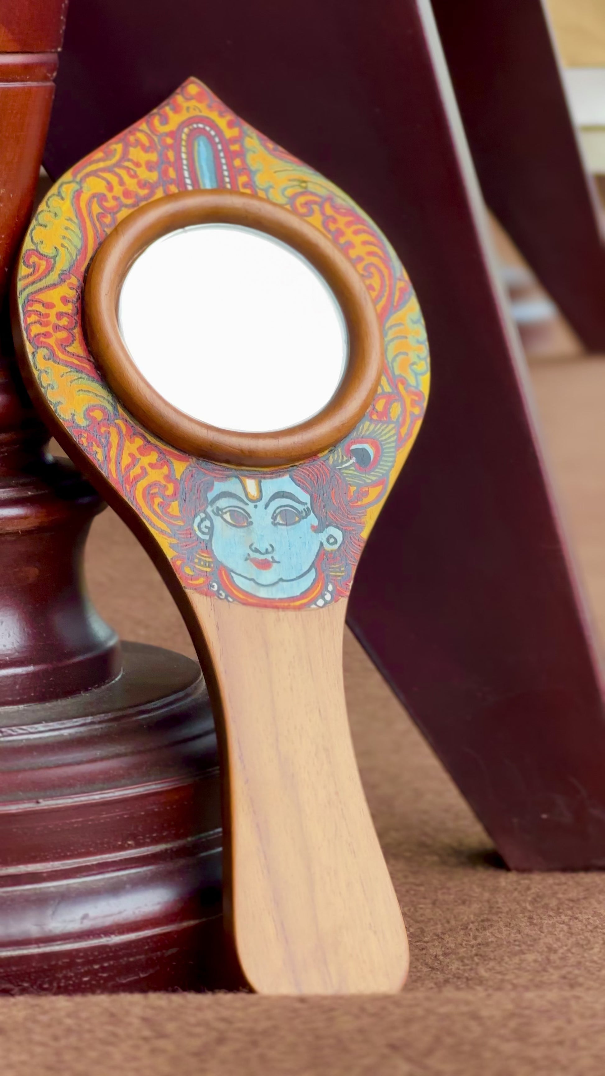 Decorative krishna hand mirror with colorful design on a dark surface