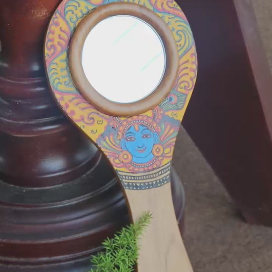 Decorative hand mirror with artistic design on a dark background