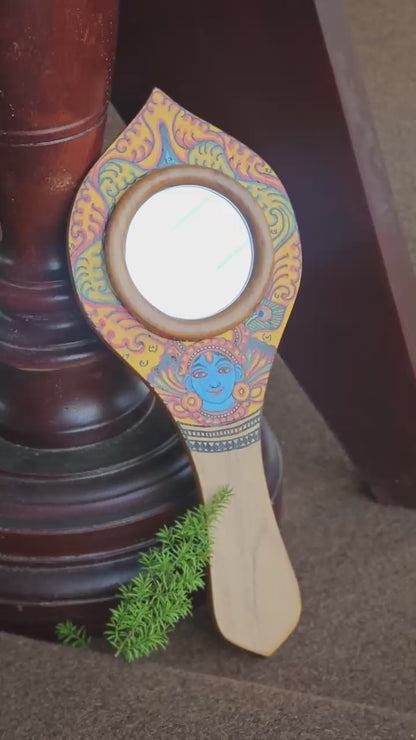 Decorative hand mirror with artistic design on a dark background