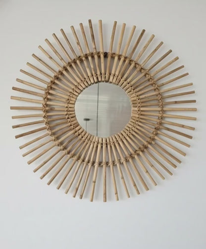 Decorative wall mirror with a sunburst design made of wooden sticks on a white wall.