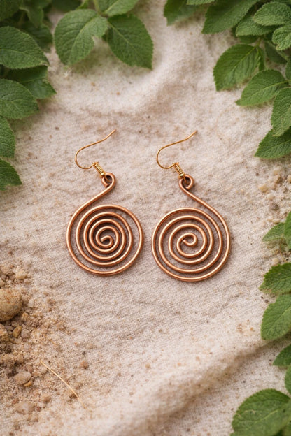 Copper spiral earrings on a textured stone surface with green leaves around.