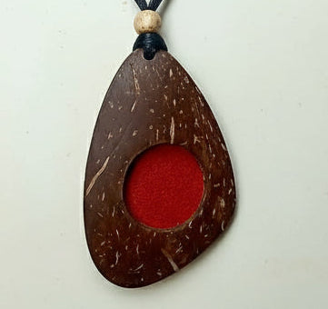 Coconut shell pendant with red center and black cord on a white background