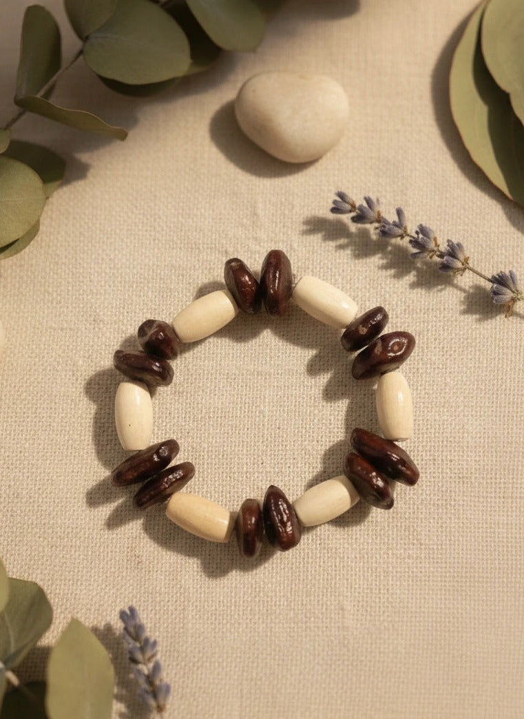 Bracelet with coffee beans and white stones on a textured surface with green leaves and lavender.