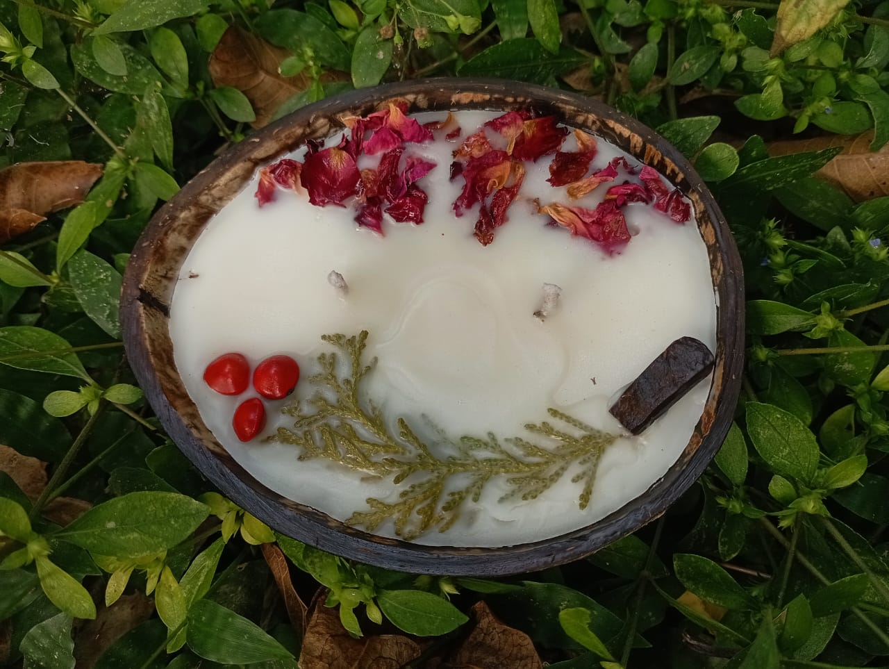 Candle in a coconut shell with natural elements on a grassy background