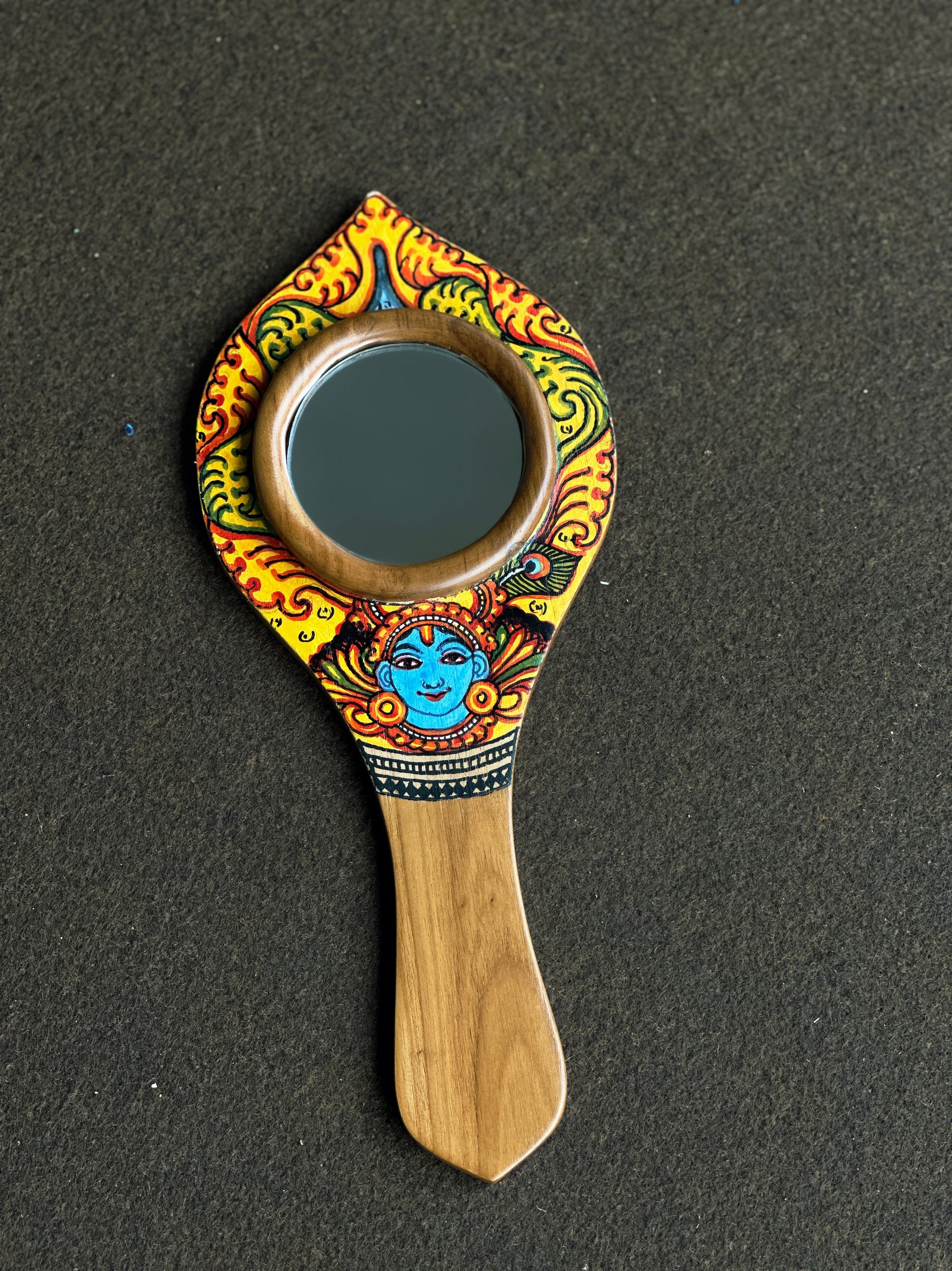 Decorative hand mirror with artistic design on a dark background