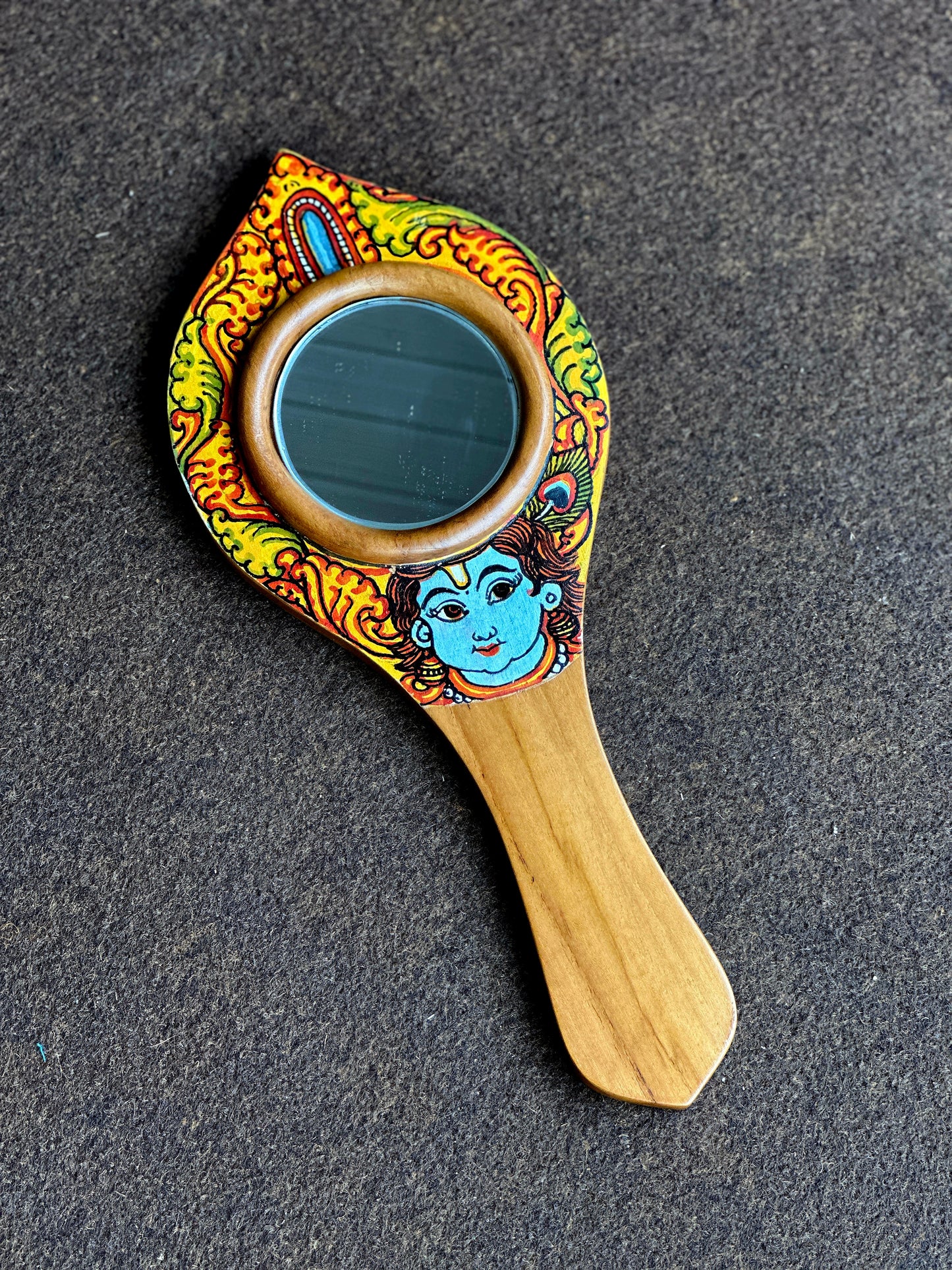 Decorative Krishna hand mirror with colorful design on a dark surface