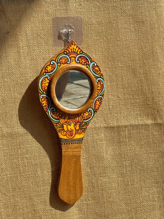 Decorative hand mirror with wooden handle and colorful design on a beige fabric background