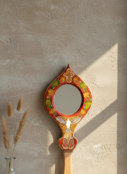 Decorative hand mirror with artistic design on a textured wall