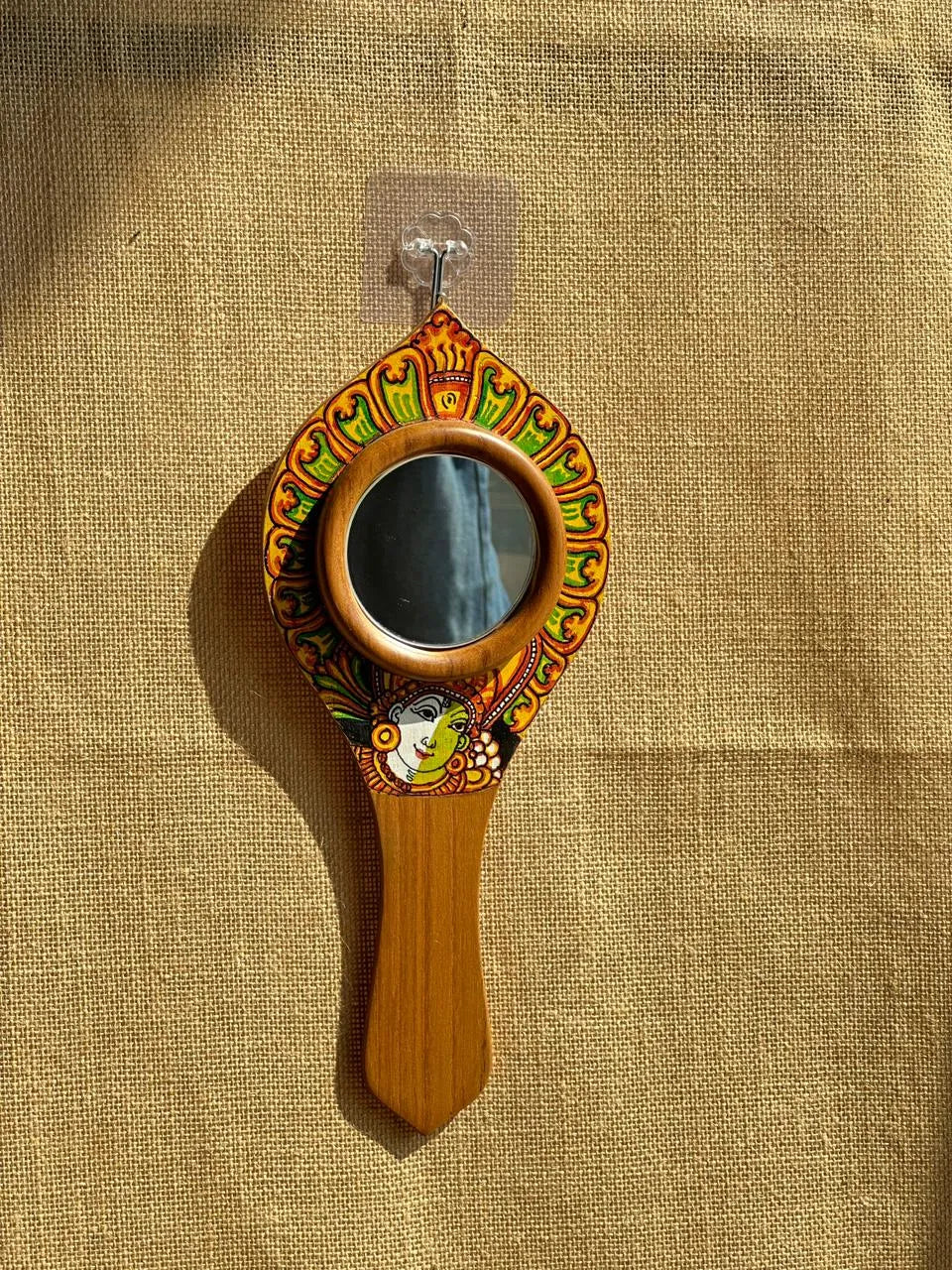 Decorative hand mirror with wooden handle and colorful frame on a beige fabric background