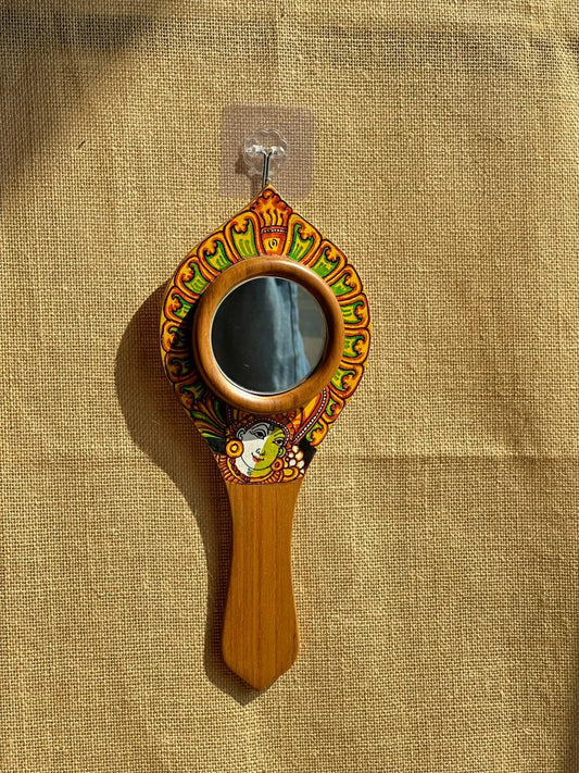 Decorative hand mirror with wooden handle and colorful frame on a beige fabric background