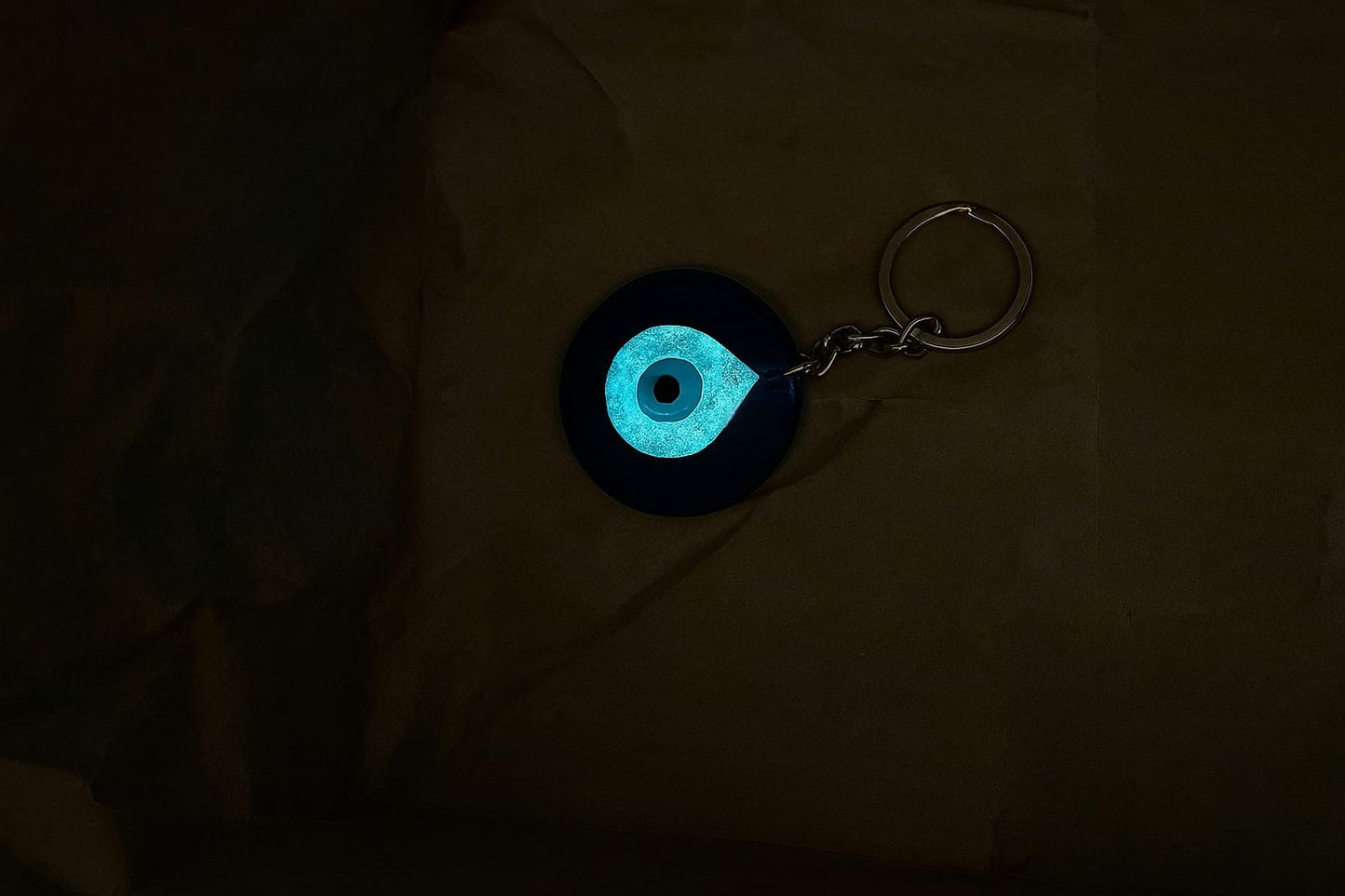 Glowing blue eye design keychain on a dark fabric background