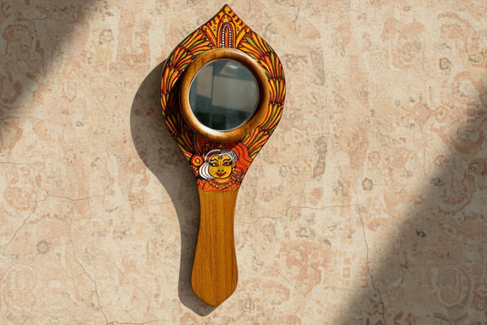 Decorative hand mirror with wooden handle and ornate design on a textured beige background