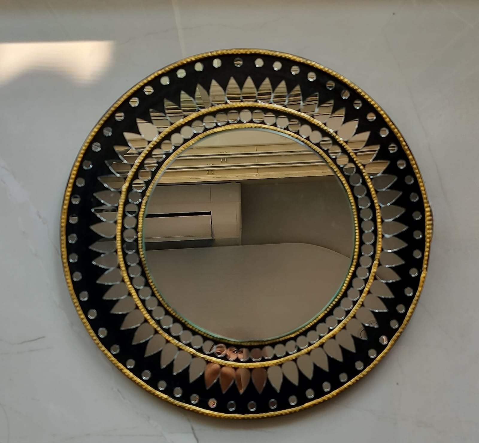 Round mirror with decorative black and gold frame on a white wall